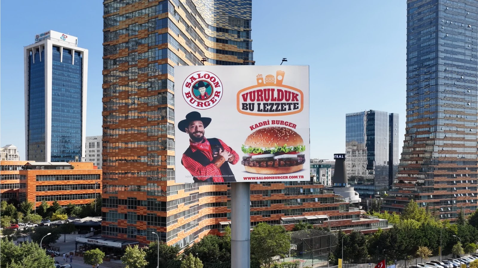 An outdoor billboard featuring a Saloon Burger campaign among the office towers of Batı Ataşehir